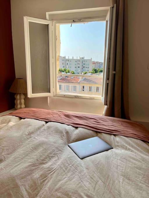- un livre sur un lit dans une chambre avec fenêtre dans l'établissement «Entre Terre et Mer » 5mins à pied Plage/15mins Vieux Port, à Marseille
