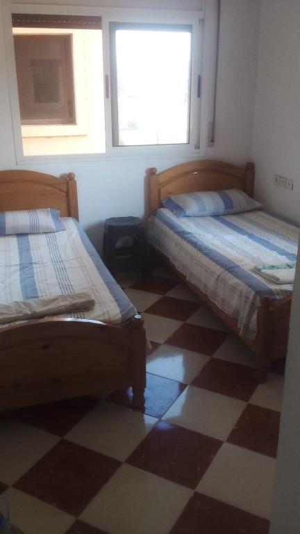two beds in a room with a checkered floor at 06ber26kane82 en face 96 carrefour06 in Berkane