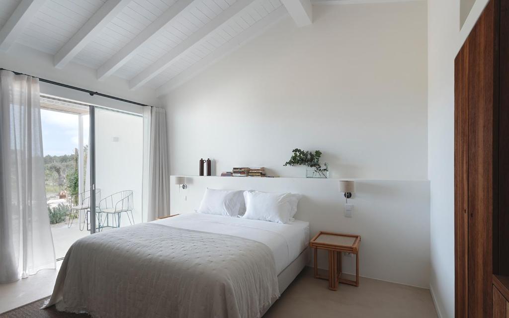 a white bedroom with a bed and a large window at Amaria in Aljezur