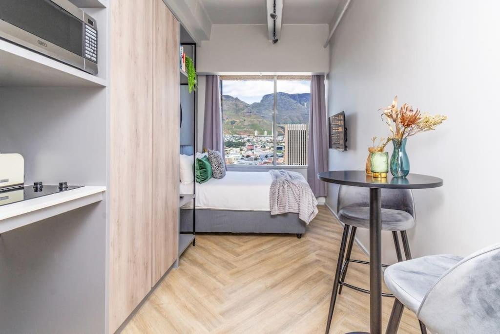 ケープタウンにあるStylish Studio Apartmentのベッド、テーブル、窓が備わる小さな客室です。