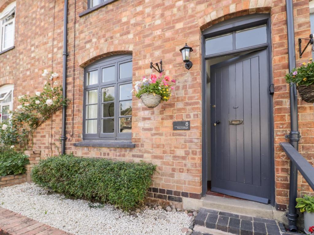 a brick house with a black door and a basket of flowers at Ross Cottage in Evesham