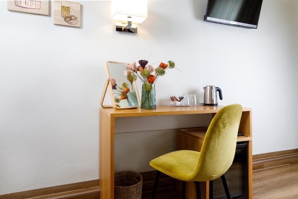 a desk with a yellow chair and a vase of flowers at Hotel am Peterstor in Regensburg
