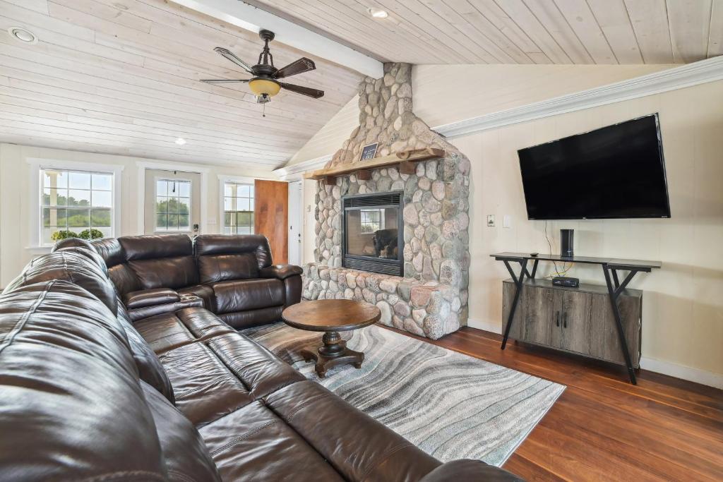 a living room with a leather couch and a stone fireplace at Lakefront Gladwin Vacation Rental with Deck and Dock! in Gladwin