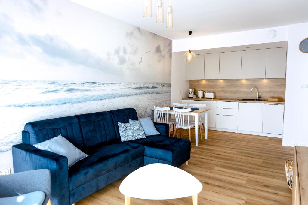 ein Wohnzimmer mit einem blauen Sofa und einer Küche in der Unterkunft Apartament z Mewami - Dziwnów Bridge Apartaments & Spa in Dziwnów