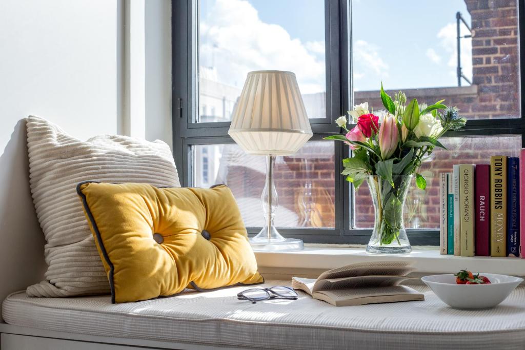 żółtą poduszkę siedzącą na siedzeniu przy oknie z wazonem kwiatów w obiekcie Chic 1BR Central London Retreat w Londynie
