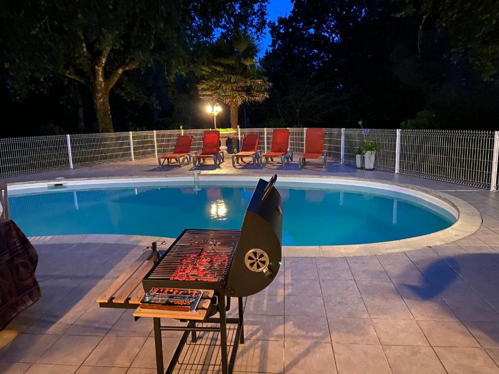una barbacoa junto a una piscina por la noche en villa 8 personnes ô Mes Anges en Saint-Julien-en-Born