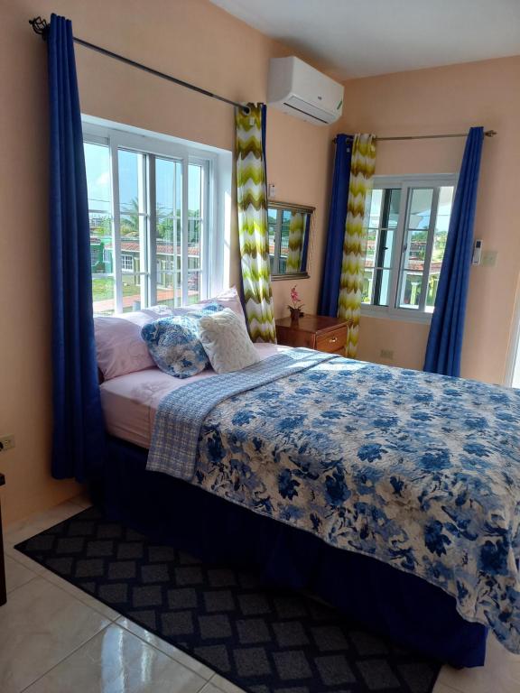 a bedroom with a bed with blue curtains and a window at Sevelle Meadows 2 Extended Stay in Spanish Town