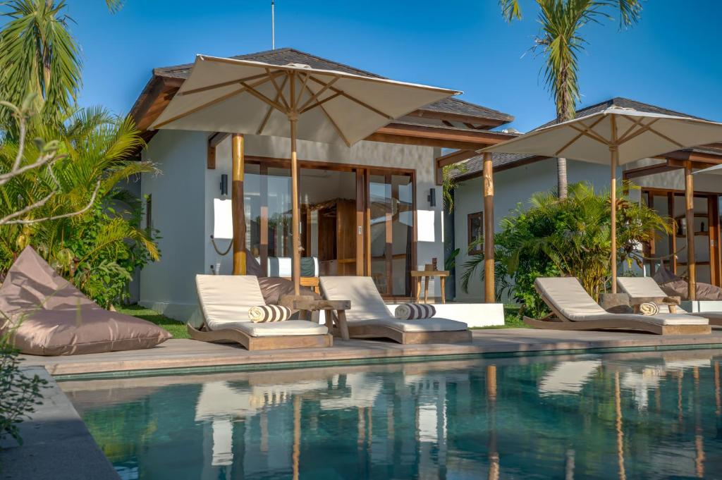 a pool with chairs and umbrellas next to a house at EHOA BALI Nyanyi Boutique Hotel - In front of entrance to NUANU in Tanah Lot