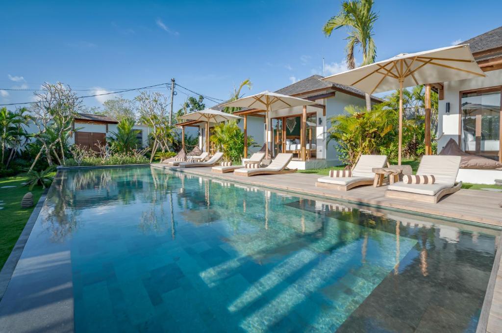 a swimming pool with white chairs and a house at EHOA BALI Nyanyi Boutique Hotel - In front of entrance to NUANU in Tanah Lot
