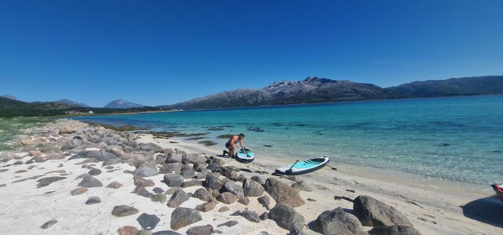 a woman standing on a beach with a surfboard at Cottage with seaview in Lødingen