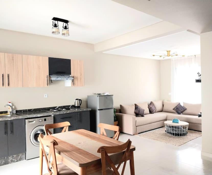 a kitchen and living room with a table and a couch at Appartement cosy proche Aéroport in Deroua