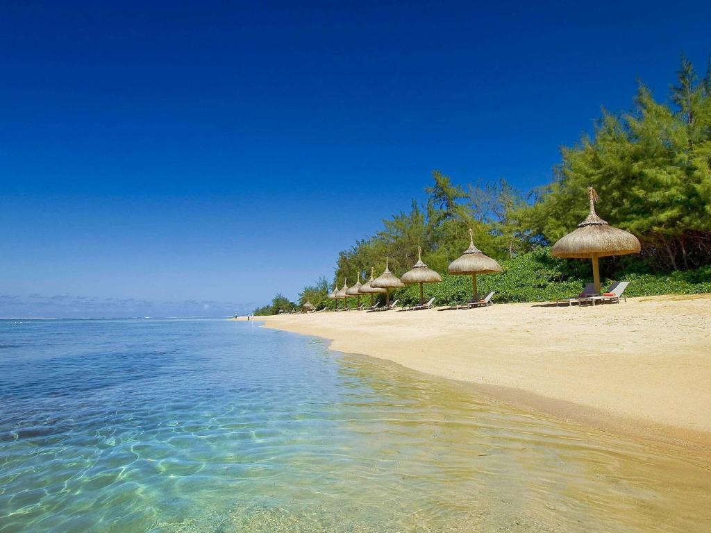 una playa con sombrillas de paja y agua en SO/ Sofitel Mauritius, en Bel Ombre