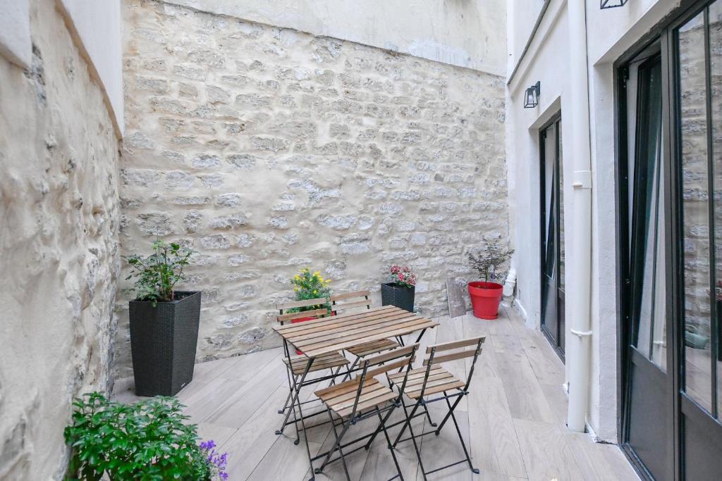 d'une terrasse avec une table et des chaises en bois ainsi qu'un mur en pierre. dans l'établissement Parking Gratuit - Montmartre Charme & Patio Privé - Sacré-Cœur Metro Anvers, à Paris