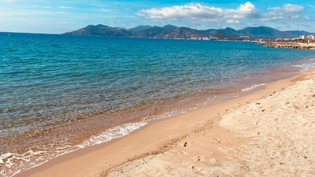 une plage avec de l'eau bleue et des montagnes en arrière-plan dans l'établissement Cosy 3pièces à 5min de la plage, à Cannes
