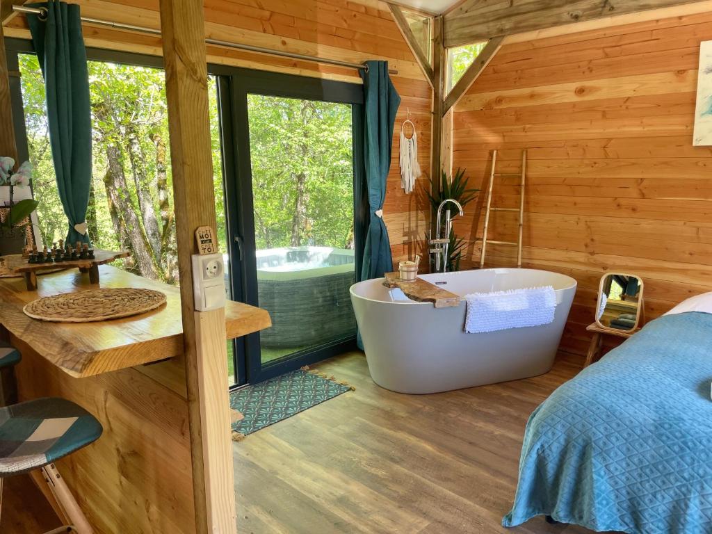 a bathroom with a tub and a bed and a window at Chalet Dalo cosy spa privé in Roussayrolles