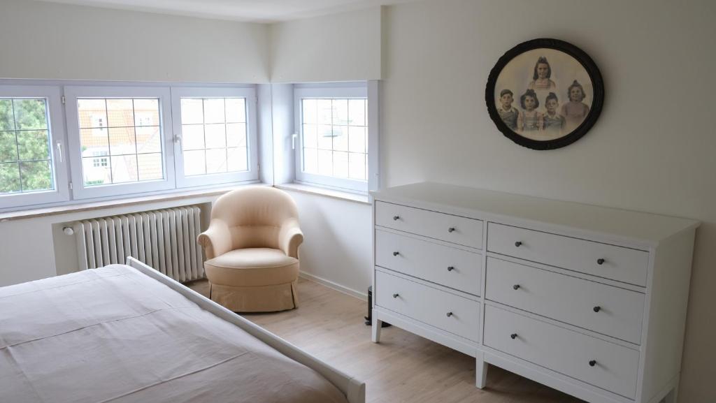 a white bedroom with a white dresser and a chair at Villa Le Renard in Knokke-Heist