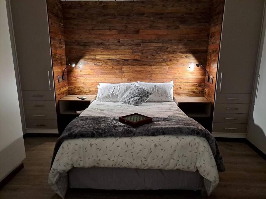 1 dormitorio con 1 cama grande y pared de madera en Mossie Nes - Self Catering, en Bloemfontein