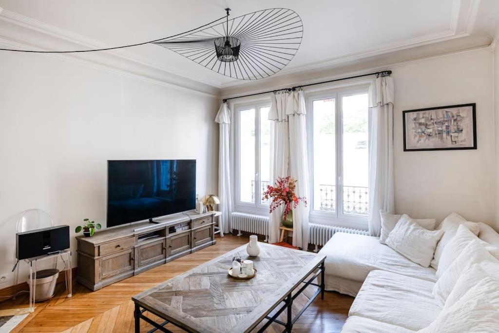 een woonkamer met een witte bank en een tv bij Charmant Appartement avec Jardin in Suresnes