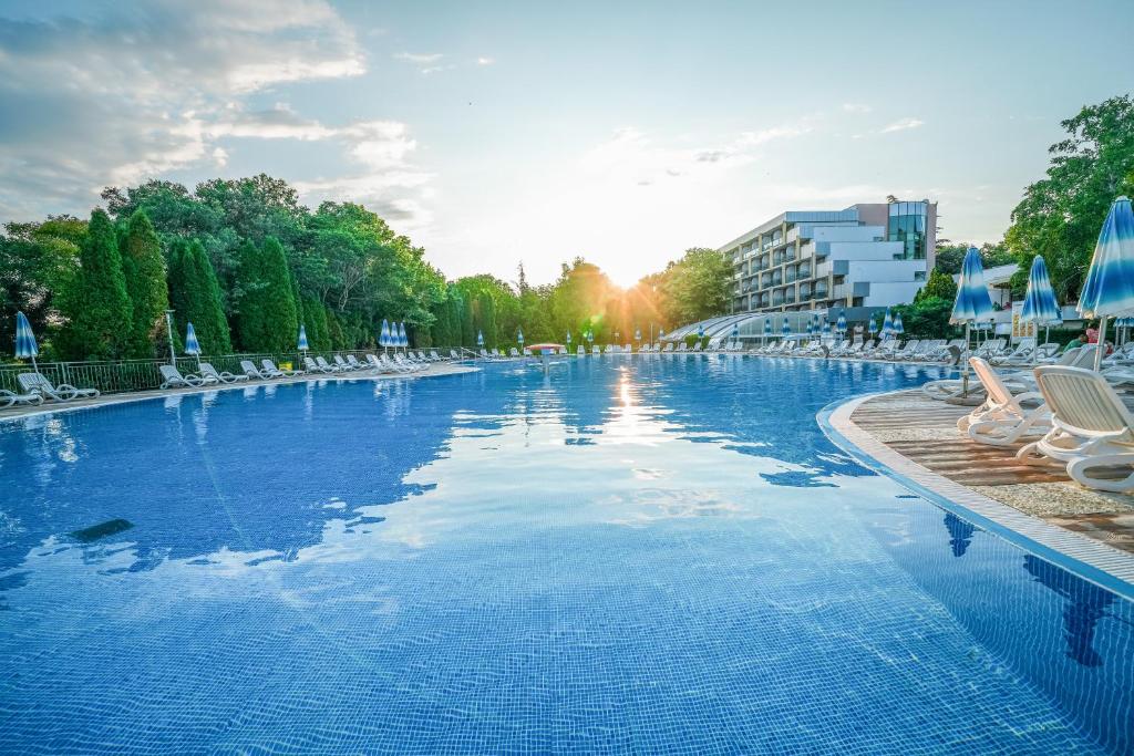 a large swimming pool with chairs and the sun setting at Calimera Ralitsa Superior Hotel - Ultra All Inclusive plus Aquapark in Albena