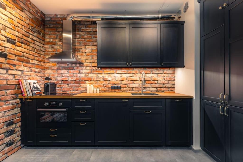 una cocina con armarios negros y una pared de ladrillo en Stunning loft-style apartment en Varsovia