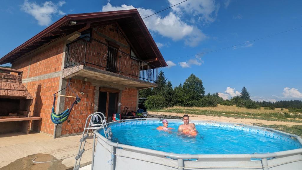 two people in a swimming pool next to a building at Vikendica Pašter in Šipovo