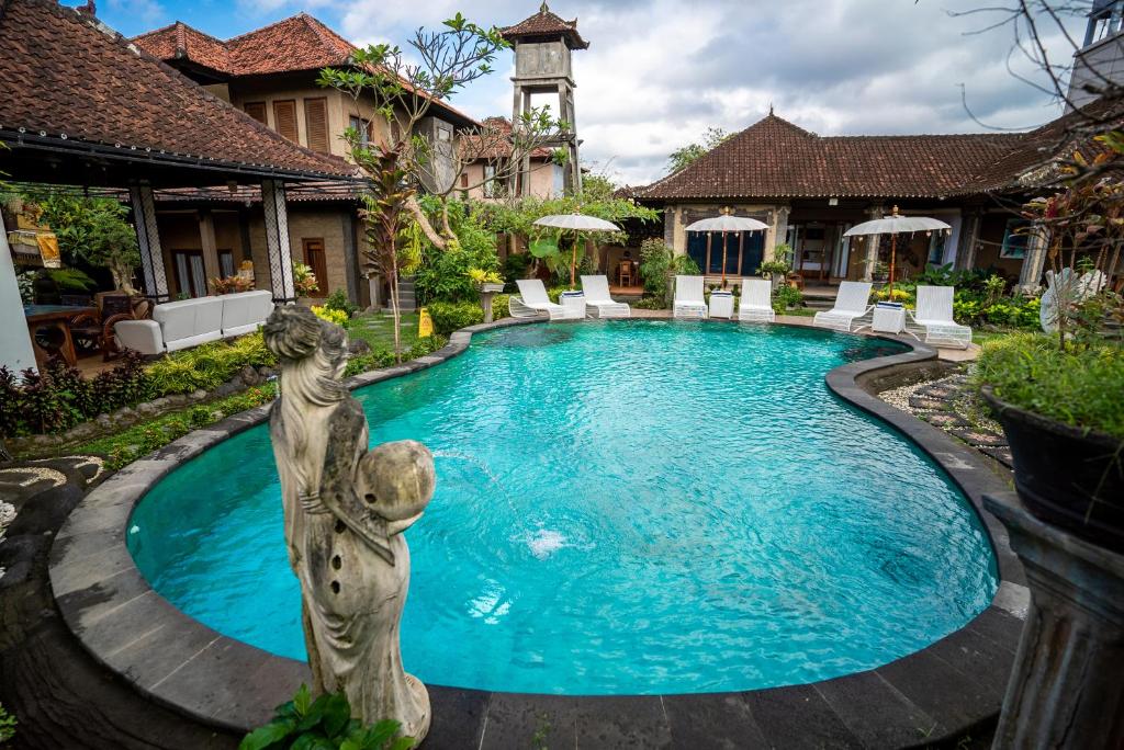 a swimming pool with a statue in front of a house at Capung Cottages in Ubud