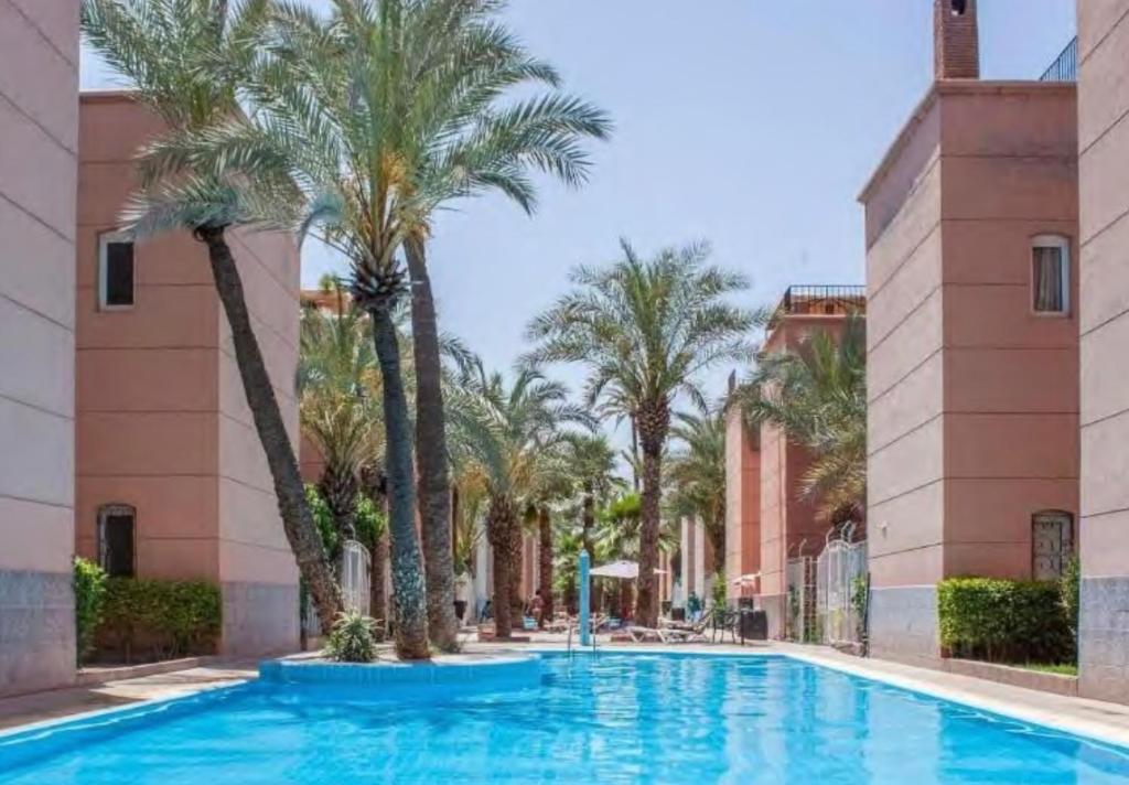a swimming pool with palm trees in front of a building at Riad Nour Beldi - Nice house near Medina in Marrakesh