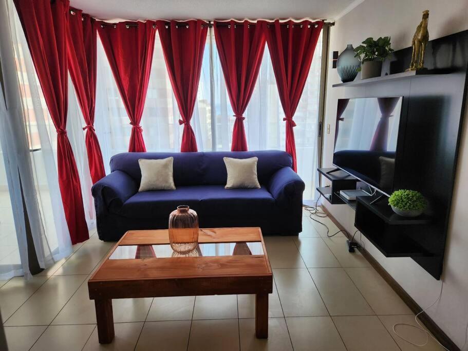 a living room with a blue couch and red curtains at Cómodo departamento diario. in Iquique