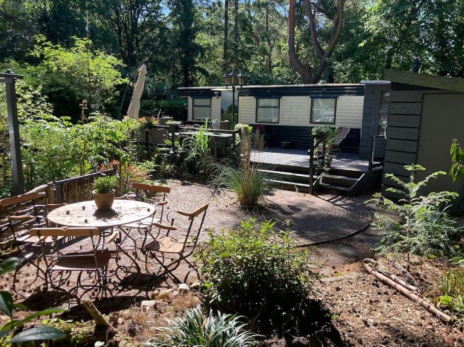 een tuin met een tafel en stoelen en een caravan bij Sfeervol chalet in het bos in Nunspeet
