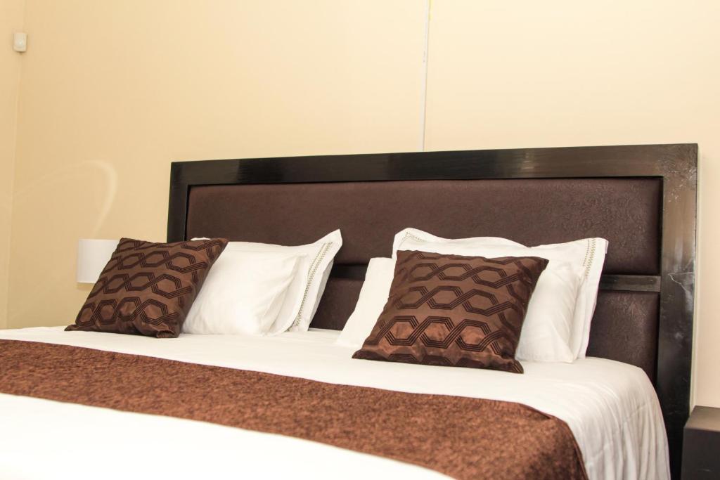 Bett mit braunen und weißen Kissen in einem Zimmer in der Unterkunft Streets of Gold Guest House Block 8 in Gaborone