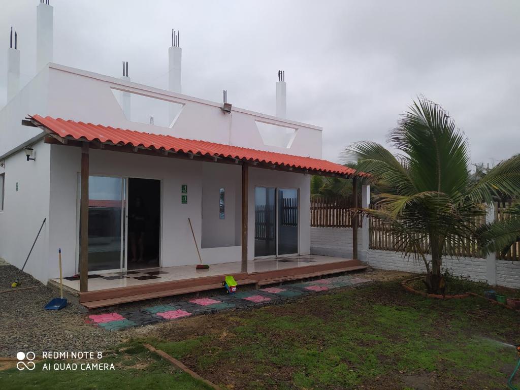 Una pequeña casa blanca con un porche y una palmera en Estancia Spondylus, en San Lorenzo