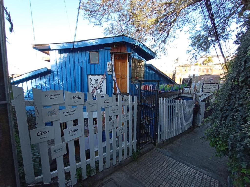 uma pequena casa azul atrás de uma cerca branca em La Casa de la Pulperia en Cerro Alegre em Valparaíso