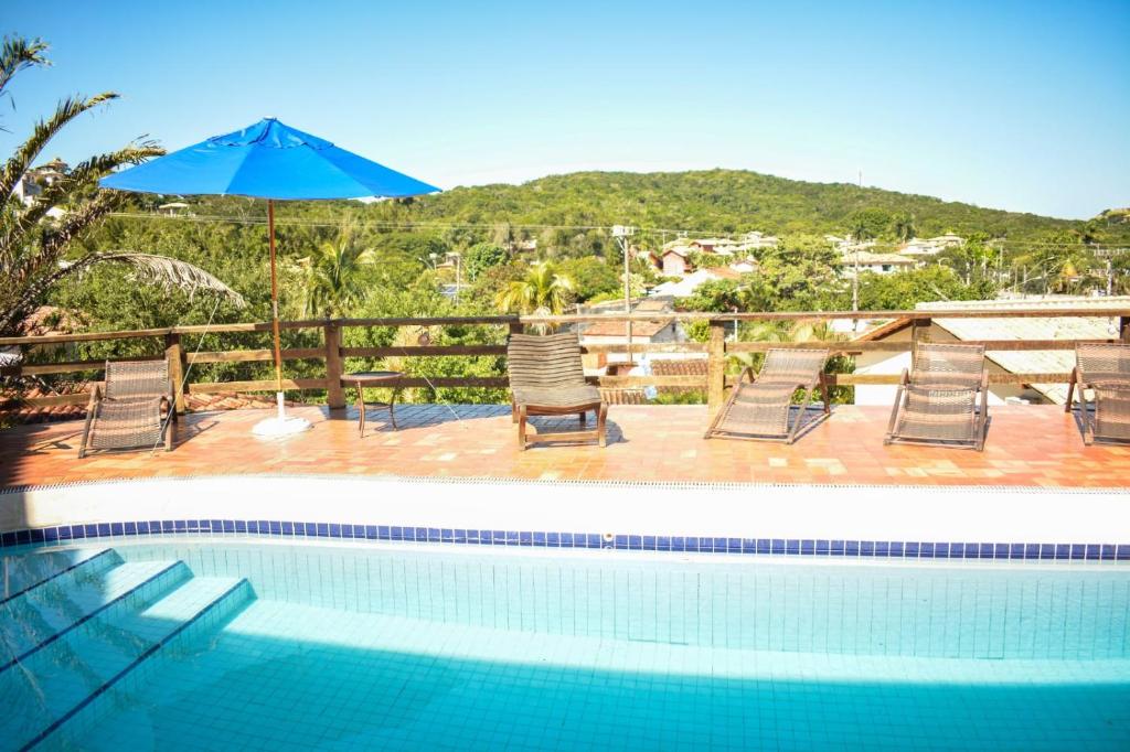 a swimming pool with chairs and a blue umbrella at Toca Geribá in Búzios