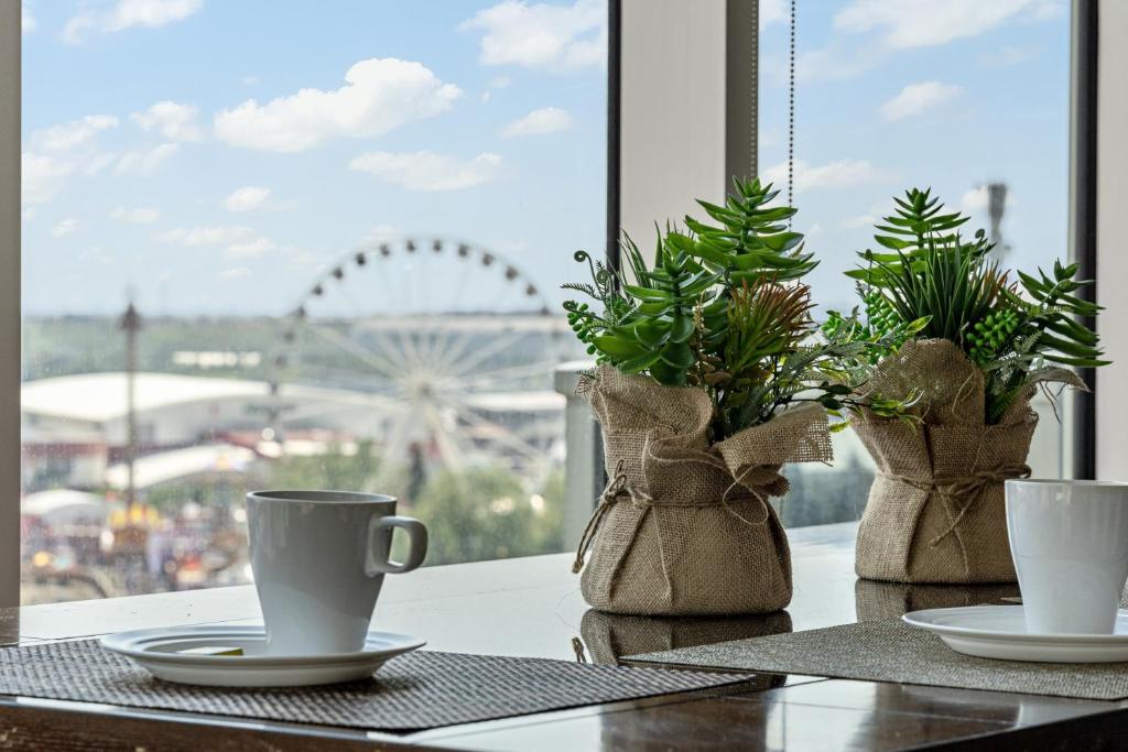 a table with two cups and potted plants on it at Chic 2BR Condo in Vibrant Downtown Calgary in Calgary