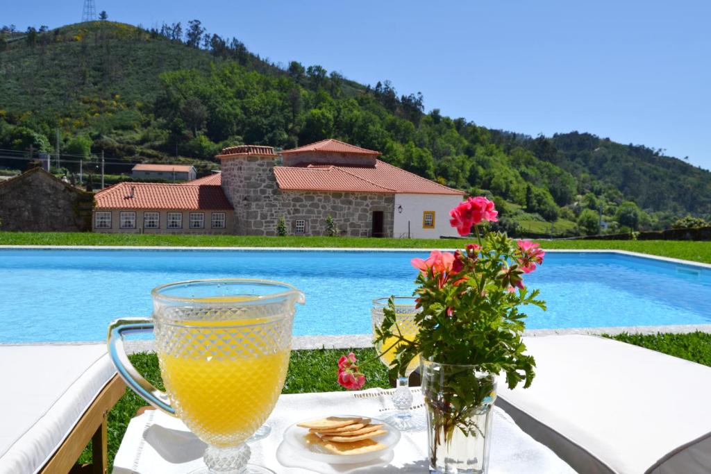 a glass of orange juice sitting on a table next to a pool at Casa da Portela de Sampriz in Ponte da Barca