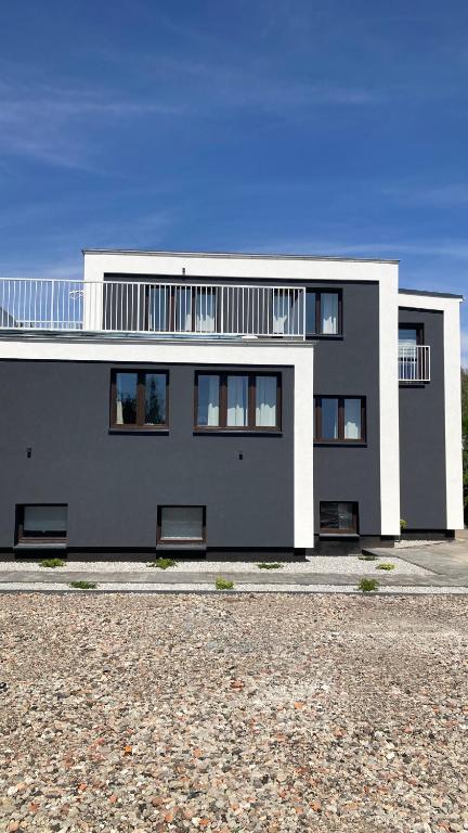 Modern dark gray building with white architectural accents and gravel forecourt under blue sky.