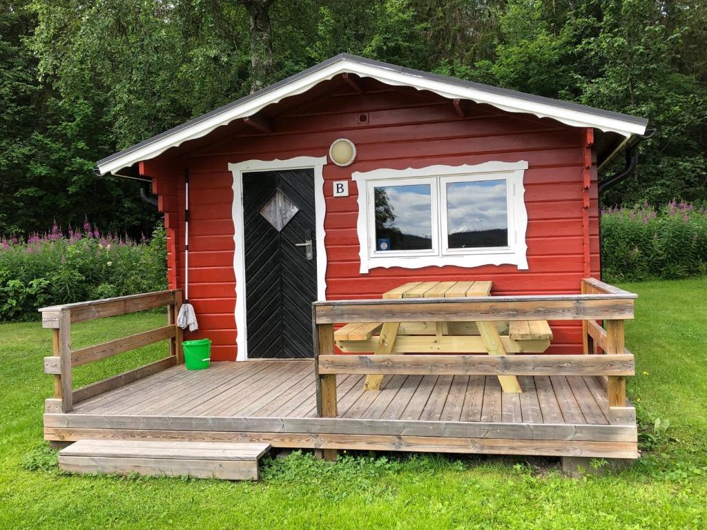 een rood bijgebouw met een houten terras in het gras bij 4 persoons Stuga in Hammarstrand