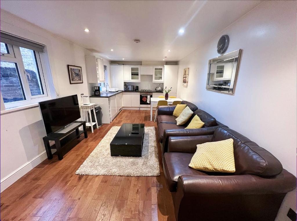 a living room with a brown leather couch and a kitchen at Lovely 2 Bedroom Garden Flat in London in London