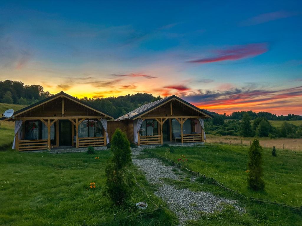 two wooden huts in a field with a sunset at Căsuțele din Poiană in Satu Şugatag