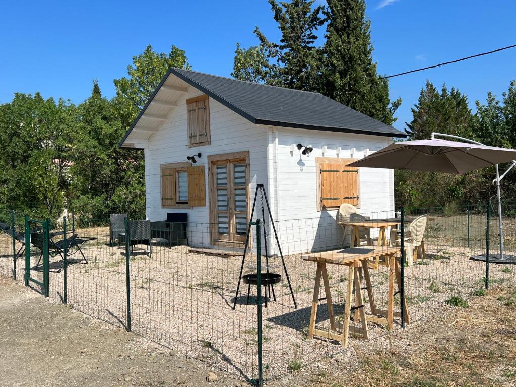 a small white shed with a table and an umbrella at Tiny-House Chalet Al måjhinete in Lodève