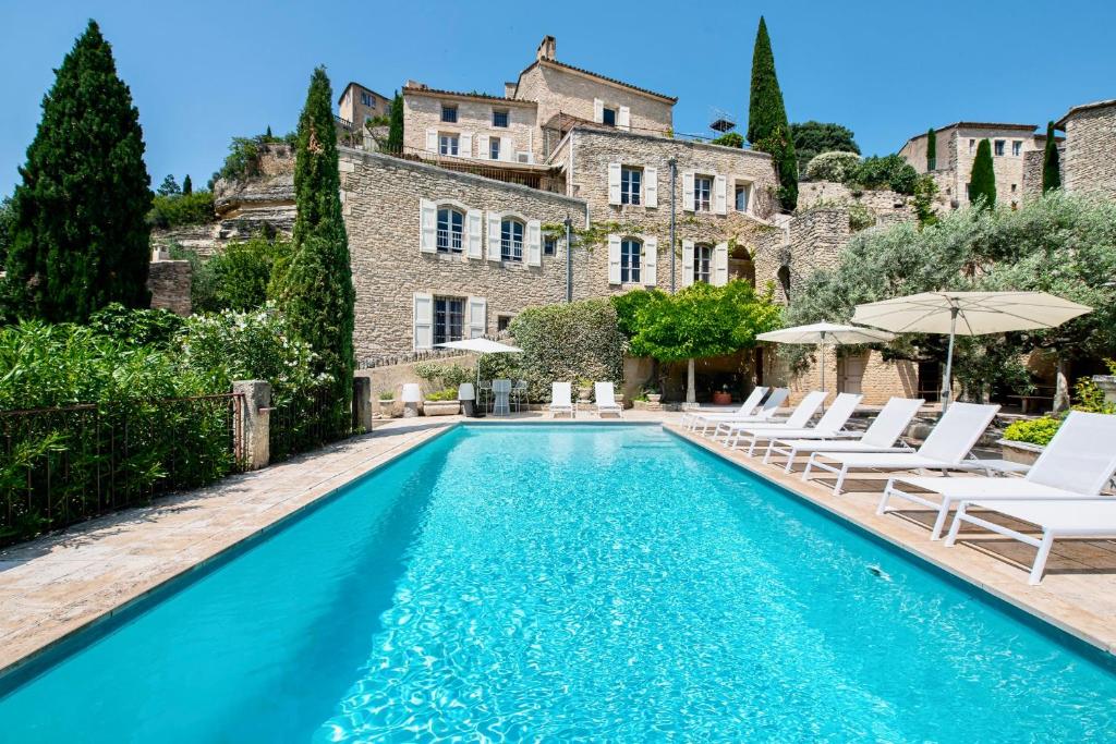 Una piscina frente a una casa con sillas blancas y sombrillas. en Le Mas Victoria, en Gordes