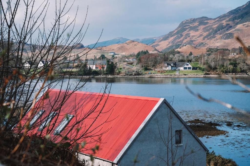 a building with a red roof next to a body of water at An Dòbhran - luxury self-catering in Dornie