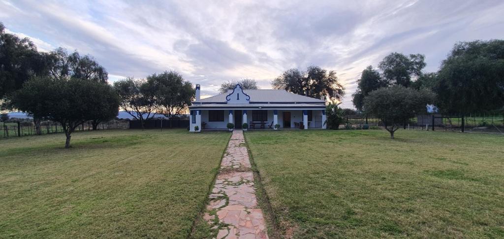 a large white house in a field with trees at Karoo Leeu Self Catering in Oudtshoorn