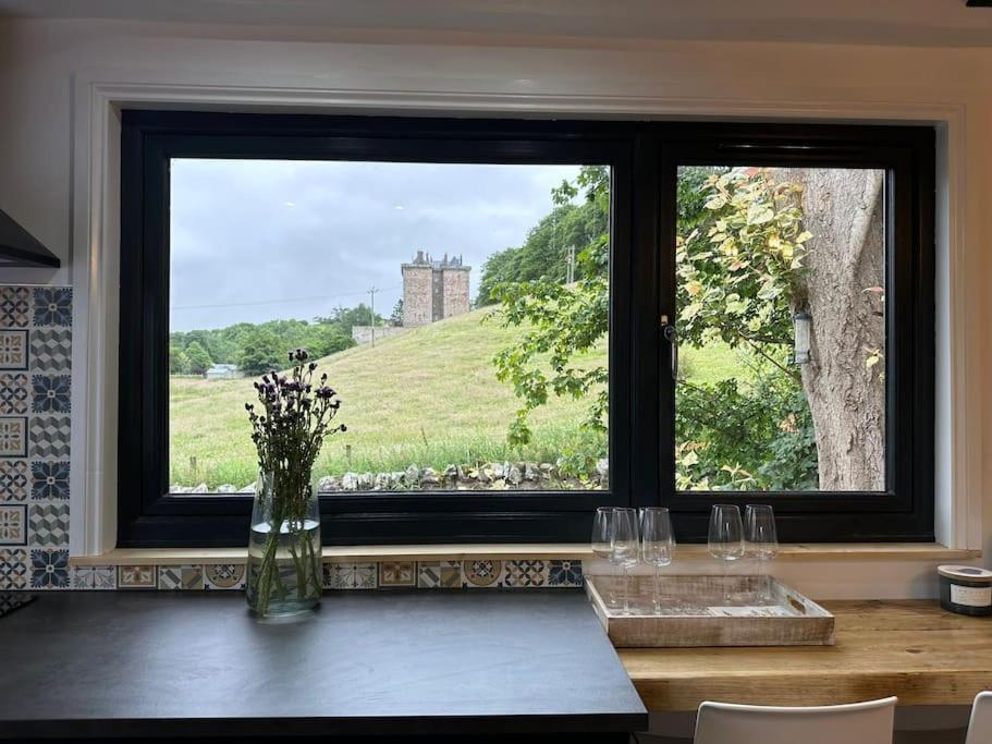 eine Vase von Blumen, die auf einem Tisch vor einem Fenster sitzt in der Unterkunft Borthwick Farm Cottage Pottery in Borthwick