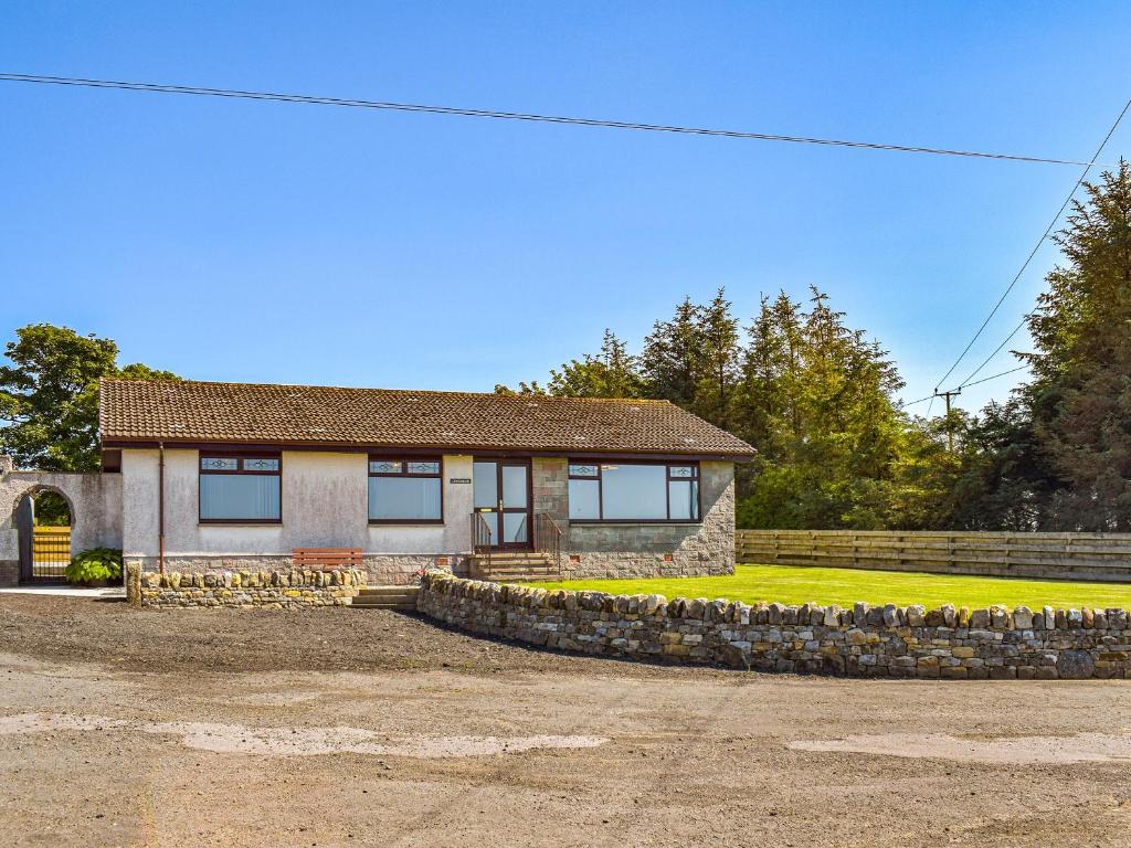 una casa con una pared de piedra de retención delante de ella en Lowesmuir Cottage, en Cumnock