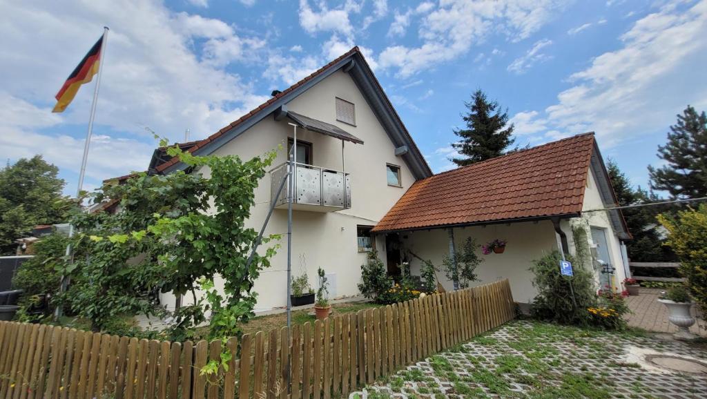 a white house with a fence and a flag at Ferienwohnung nähe Bodensee. in Meckenbeuren