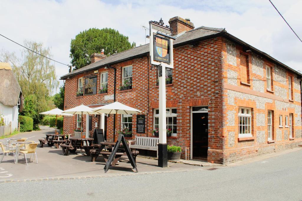 a brick building with tables and umbrellas in front of it at The George Inn St Mary Bourne in Saint Mary Bourne