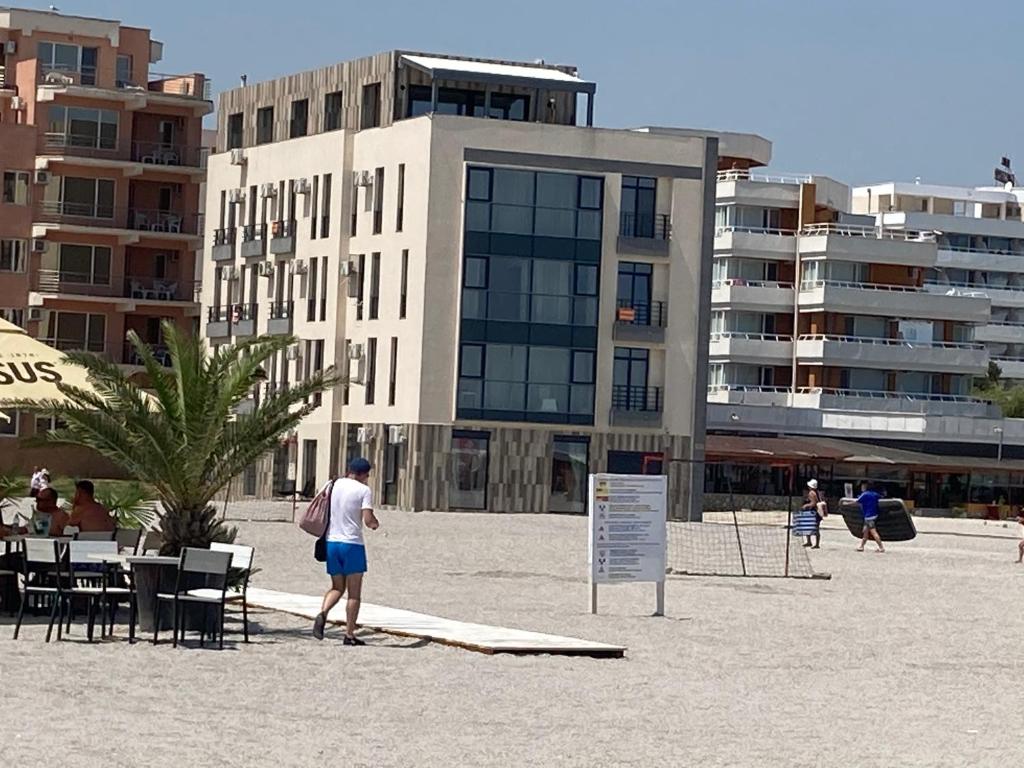 Un uomo in piedi sulla spiaggia di fronte a un edificio di Beach Rooms Roberta a Mamaia