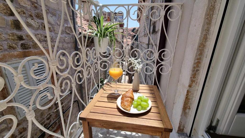 a table on a balcony with a plate of food and an orange juice at Mascheroni Luxury Rooms in Dubrovnik