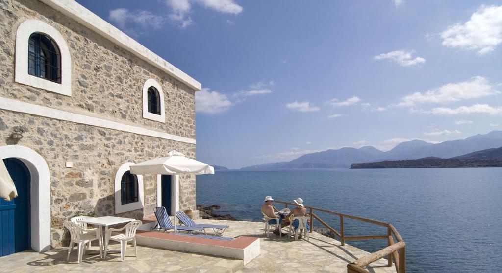 dos personas sentadas en un patio cerca del agua en Karavostassi - The Stonehouse, en Agios Nikolaos